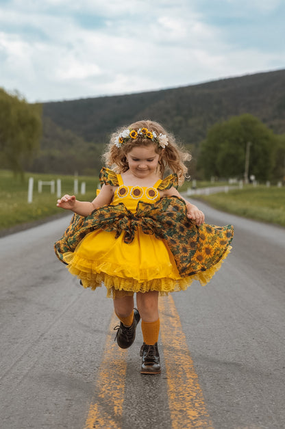 Child in a yellow dress with sunflower pattern running on a road with greenery in the background
